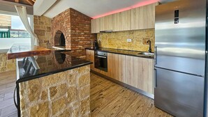 Eine Küche mit Backofen aus Ziegeln, Holzschränken, einem Edelstahlkühlschrank und einer Steinen Insel.