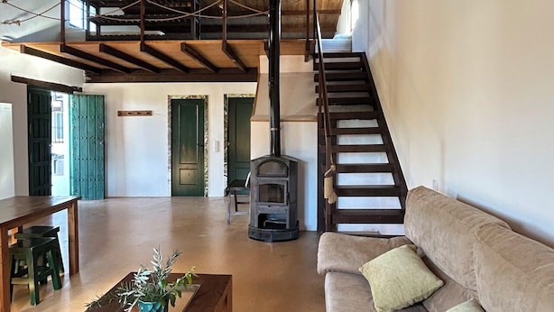 Amplia sala de estar con una escalera de madera, un sofá con cojines, una mesa de centro de madera y una chimenea.