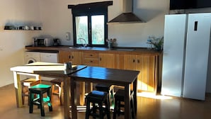 Una cocina con armarios de madera, un refrigerador blanco, un microondas y una ventana con vista a árboles.