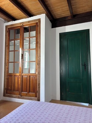 Habitació amb armari de fusta, porta verda i llit amb mantell estampat.