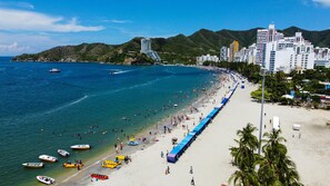 A beach with boats, a long stretch of beach umbrellas, and a cityscape in the background. - Luxury Ocean View Apartment in Rodadero (El Rodadero)