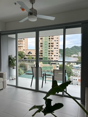 A spacious room with a large sliding glass door leading to an outdoor tennis court, a ceiling fan, and a potted plant. - Luxury Ocean View Apartment in Rodadero (El Rodadero)