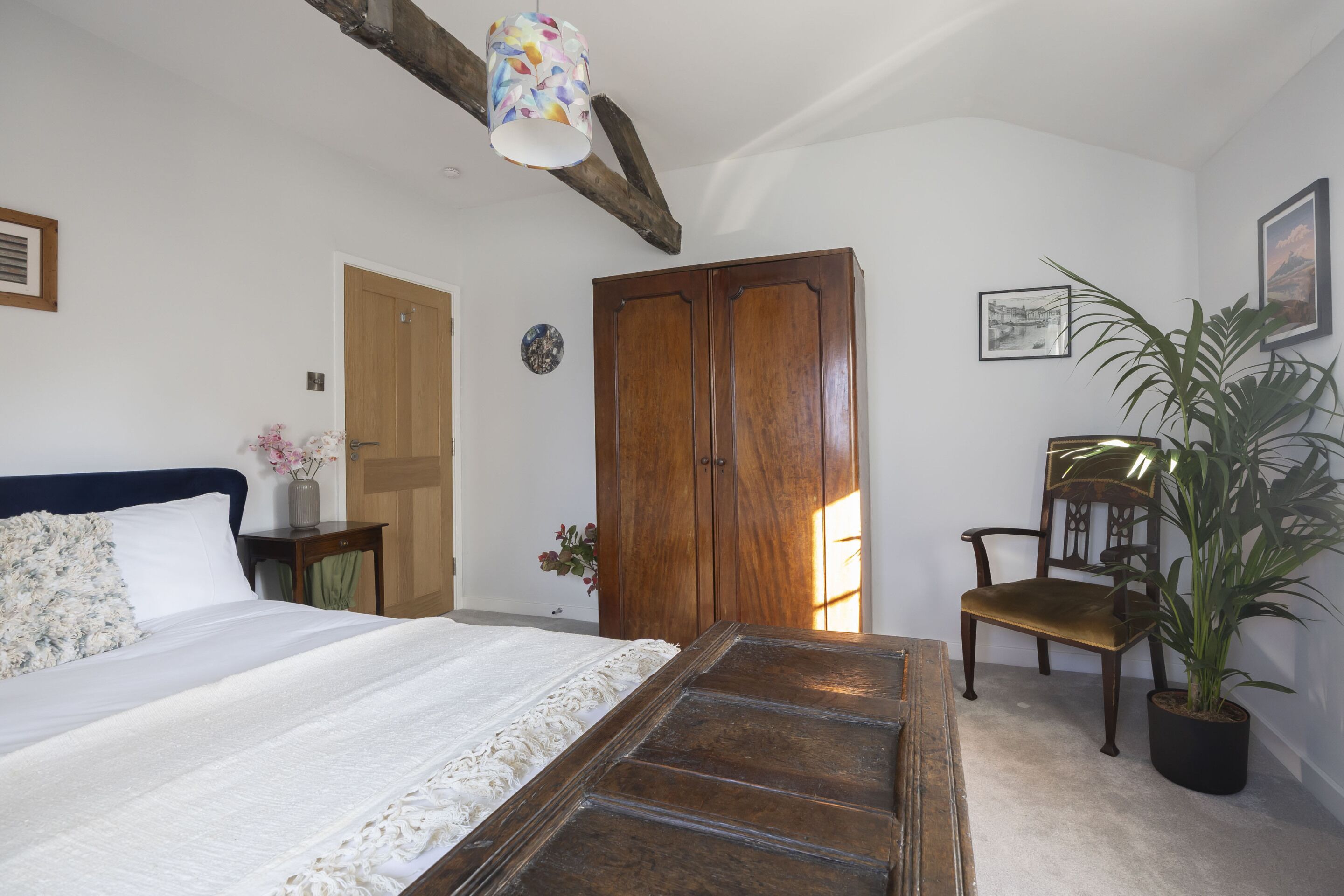 A bedroom with a bed, wooden wardrobe, chair, potted plant, and a decorative ceiling light.