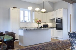 A modern kitchen with white cabinets, a central island, pendant lighting, and a patterned rug. - Beautiful Coach House in the Heart of Montpellier (Cheltenham)