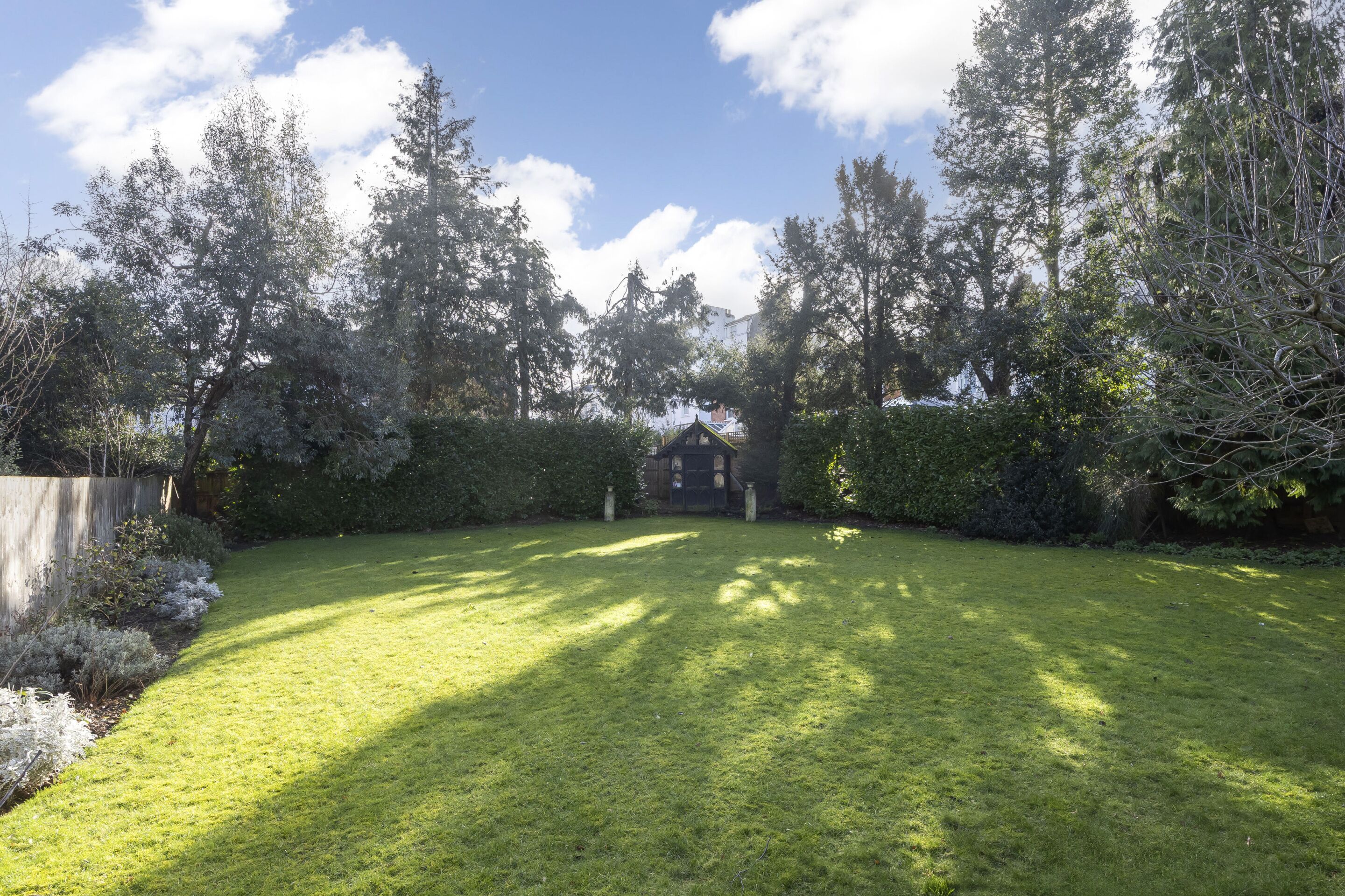A well-maintained lawn with a wooden structure in the center, surrounded by dense trees and a clear sky.