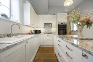 A modern kitchen with white cabinetry, granite countertops, a built-in oven, and a window with decorative plants. - Beautiful Coach House in the Heart of Montpellier (Cheltenham)