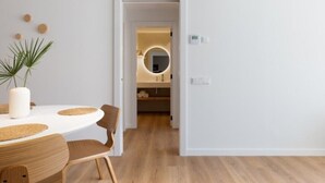Et moderne interiør med et rundt spisebord, stole, en potteplante og en døråbning ind til et badeværelse med et rundt spejl.