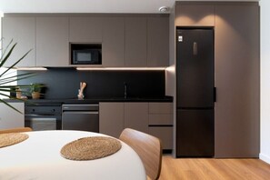 A modern kitchen with a microwave, refrigerator, and wooden cabinets. - Signature Apartment, City View with King bed (Sitges)