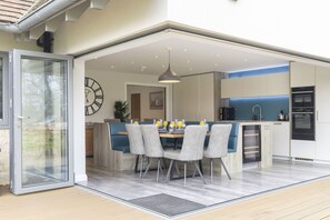 A modern kitchen with a dining area, a clock, and a sliding glass door leading to an outdoor space. - Stunning Detached Countryside Home in Cheltenham (Cheltenham)