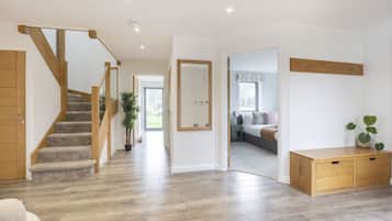 A spacious hallway with a wooden staircase, a bed with a window, and a bedside table.