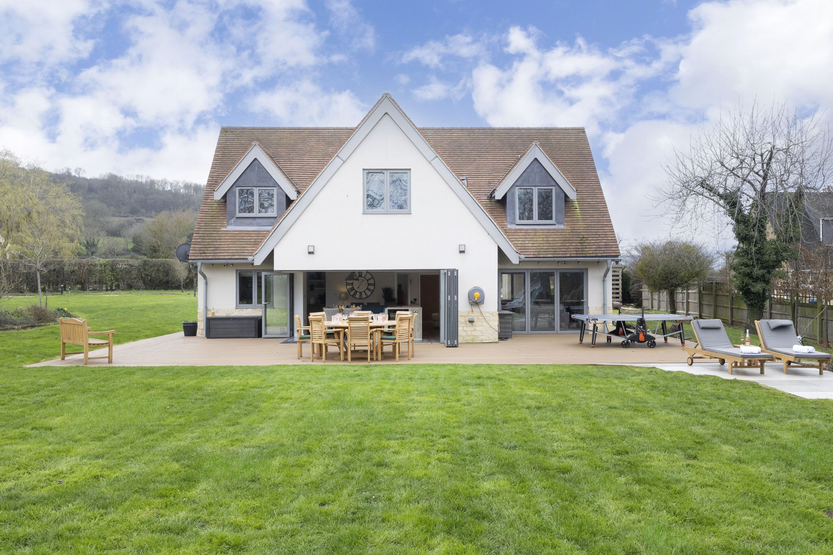 A house with a large patio, a dining area, and two lounge chairs.