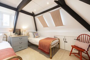 Un dormitorio con cama, mesita de noche, una silla, armario y ventana con cortinas.