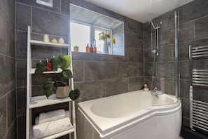 A modern bathroom with a bathtub, a shelf with toiletries, and a window with a view.