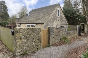 A stone house with a sloped roof, a wooden gate, and a gravel driveway.