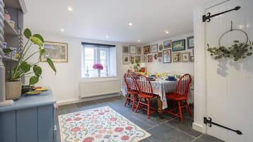 A dining area with a table and chairs, a window with a view, and a wall decorated with framed pictures.