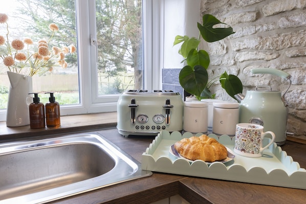 Una cocina con un tostador, una tetera, una taza y una bandeja con un croissant.