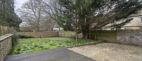 A backyard with a wooden deck, a tree, and a gravel area.
