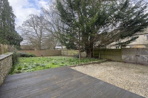 A backyard with a wooden deck, a tree, and a gravel area. - Cosy 2 Bed Cotswold Stone Cottage in Cirencester (Cirencester)
