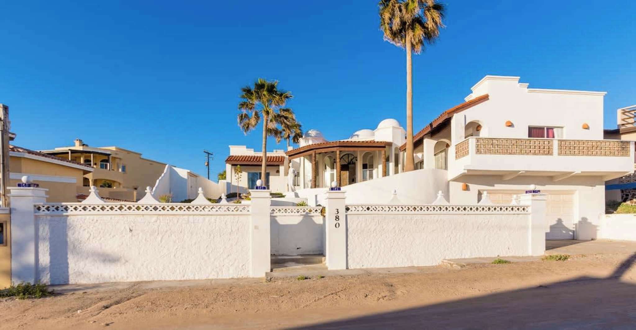 A residential area with white houses, a gated entrance, and palm trees.