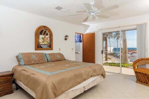 A bedroom with a bed, a ceiling fan, a window with a view of palm trees, and a door leading to an outdoor area. - Recently Renovated Oceanview Home Casa Hebe (Puerto Peñasco)