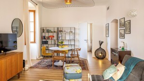 A modern living room with a TV, dining area, bookshelf, and a cozy seating area. - Casa Bianca – Charme & vue mer au cœur d’Erbalunga (Brando)