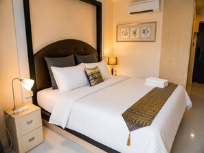 Una cama bien hecha con cabecera, una lámpara de noche, una mesita de noche con cajones y un aire acondicionado instalado en la pared.