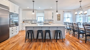 Una cocina moderna con armarios blancos, un refrigerador de acero inoxidable, una isla central con taburetes e iluminación colgante.