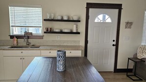 A kitchen with a dark wooden table, white cabinets, and a window with blinds. - Pleasant 1-bedroom cottage in charming Manhattan (Manhattan)