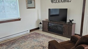 A living room with a flat-screen TV, a brown sofa, a patterned rug, a 'WELCOME' sign, and a framed picture on the wall. - Pleasant 1-bedroom cottage in charming Manhattan (Manhattan)