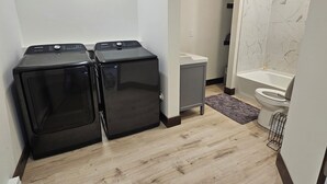 A compact bathroom with a shower, toilet, and two stacked washers. - Pleasant 1-bedroom cottage in charming Manhattan (Manhattan)