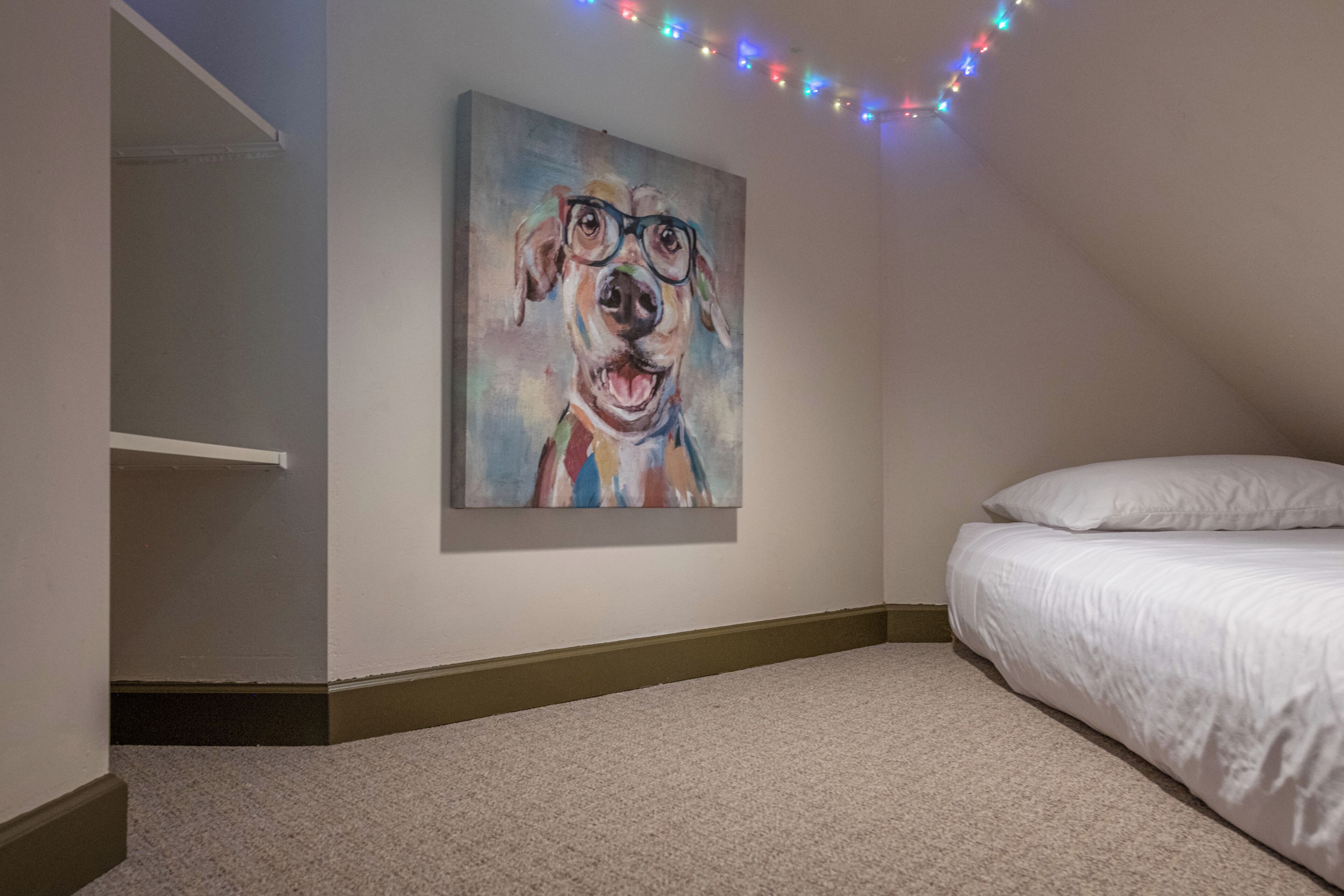 Une chambre à coucher avec un lit, un tableau accroché au mur et une guirlande lumineuse.
