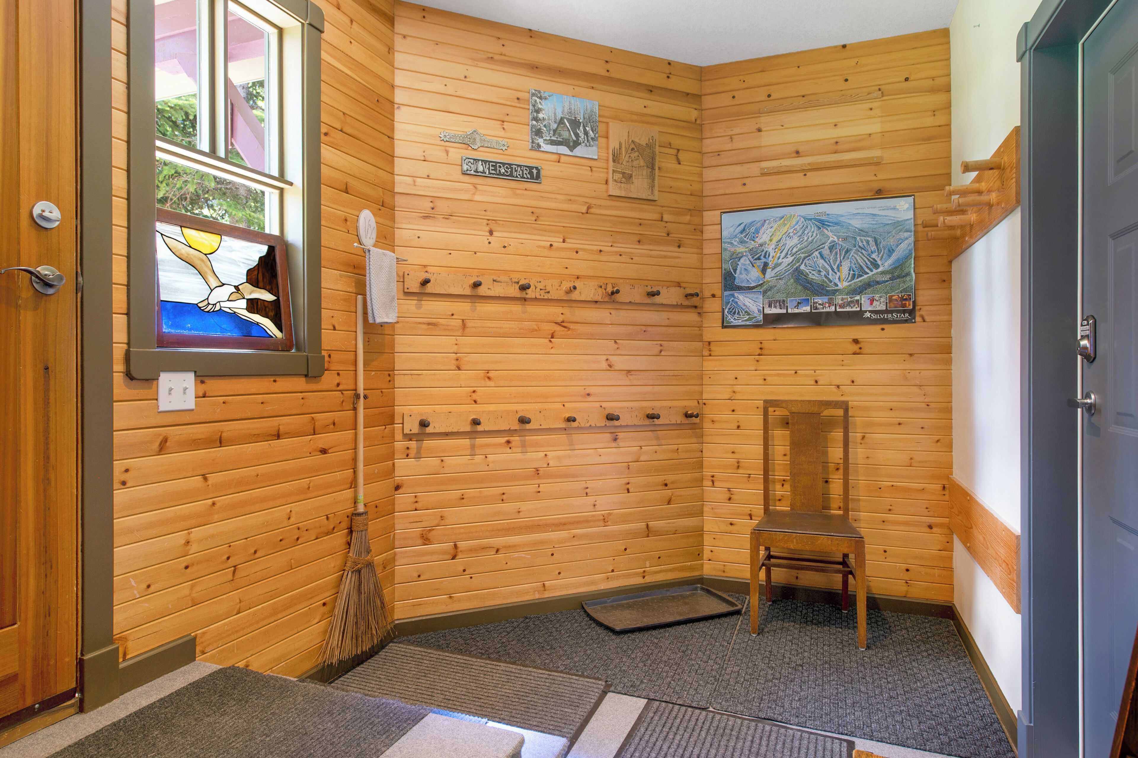 Interior de una cabaña de madera con pared de madera, un escoba, una silla y una ventana con vistas.