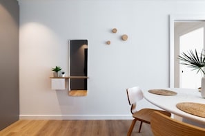 Ein moderner Essbereich mit einem weißen Tisch, Holzstühlen, einem wandmontierten Regal mit einer Pflanze und einem Spiegel.