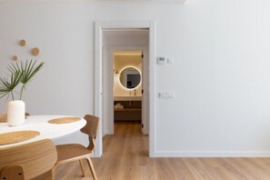 Ein modernes Interieur mit einem runden Esstisch, Stühlen, einem Blumentopf und einer Tür zu einem Badezimmer mit einem runden Spiegel.