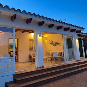 A building with a tiled roof, a balcony with chairs, and a large glass door leading to an interior space.