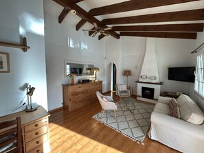 A living room with wooden beams, a fireplace, a TV, a sofa, a chair, and a wooden cabinet.