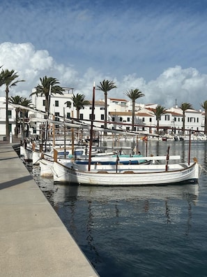 A marina with boats docked, a waterfront promenade, and white buildings with red-tiled roofs.