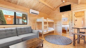 A wooden cabin interior with bunk beds, a sofa, a TV, and a window with a view. - Family Cabin in the heart of The Pennsylvania Grand Canyon (Wellsboro)