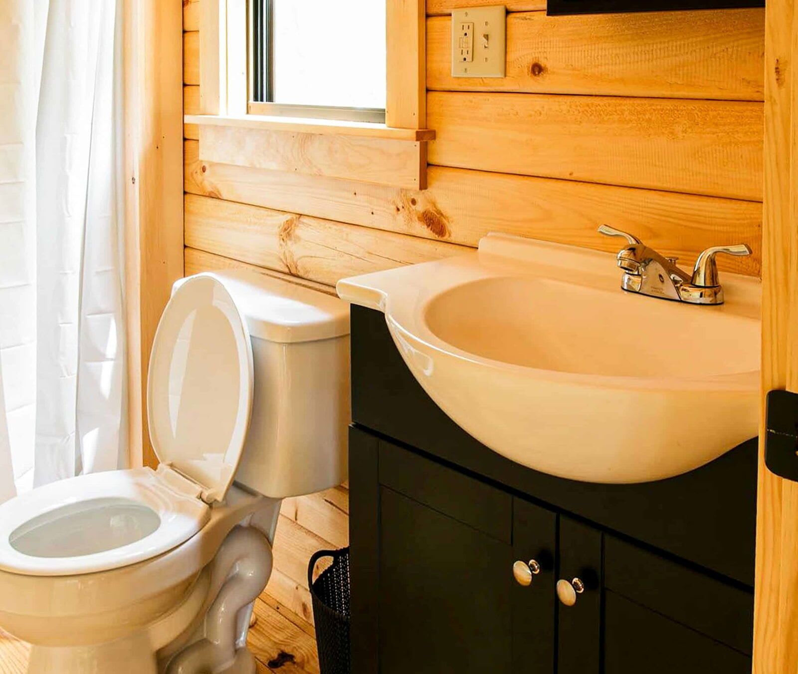 Baño de cabaña de madera con inodoro, lavabo y ventana.