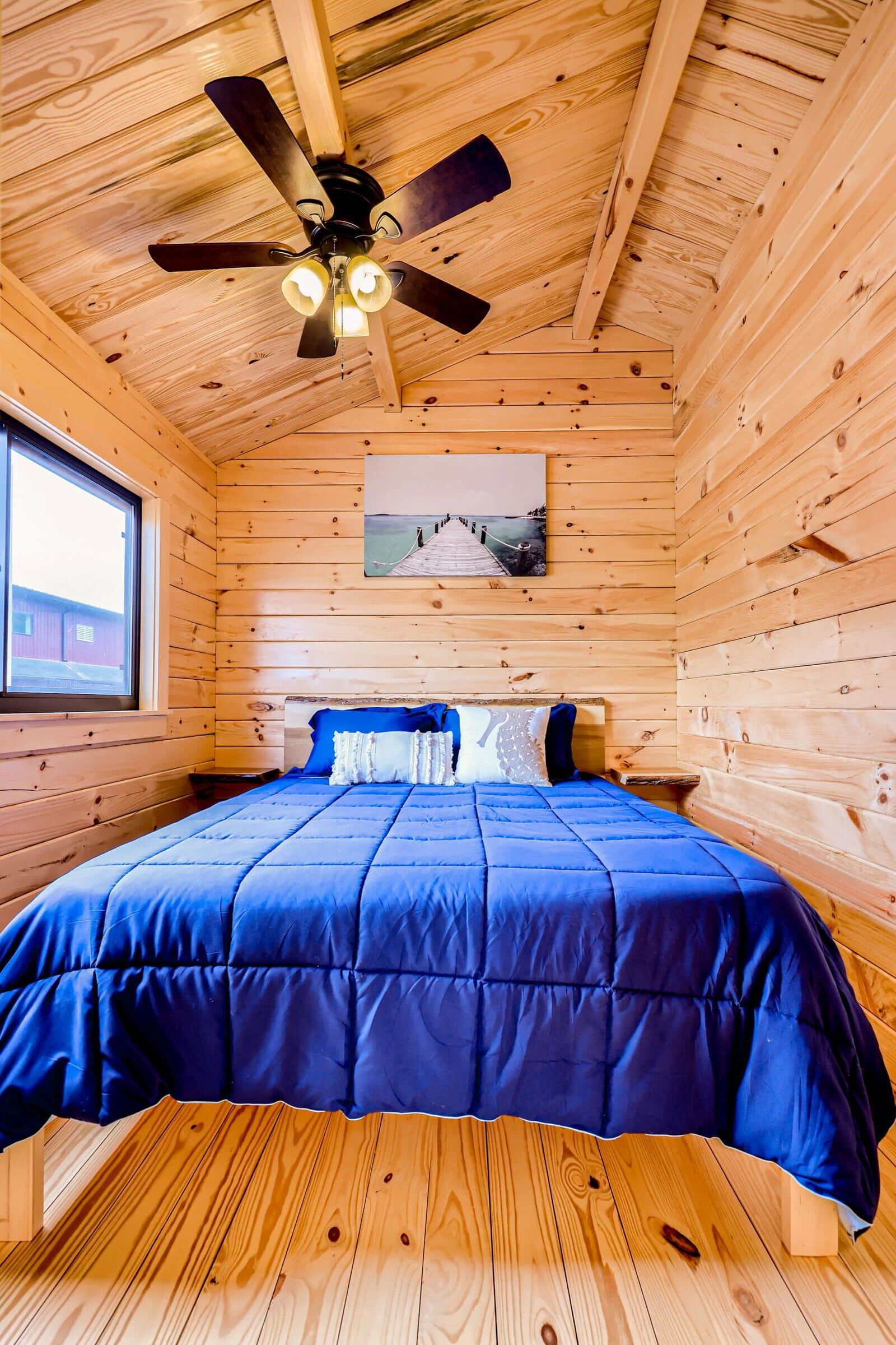 A wooden cabin bedroom with a bed, a ceiling fan, and a window.