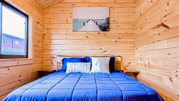 A wooden cabin bedroom with a bed, a ceiling fan, and a window.