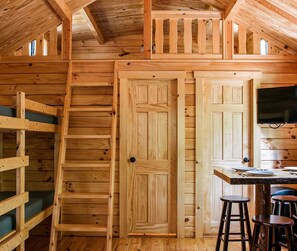 Un intérieur en bois avec un lit superposé, une table à manger avec des tabourets et un téléviseur fixé au mur.