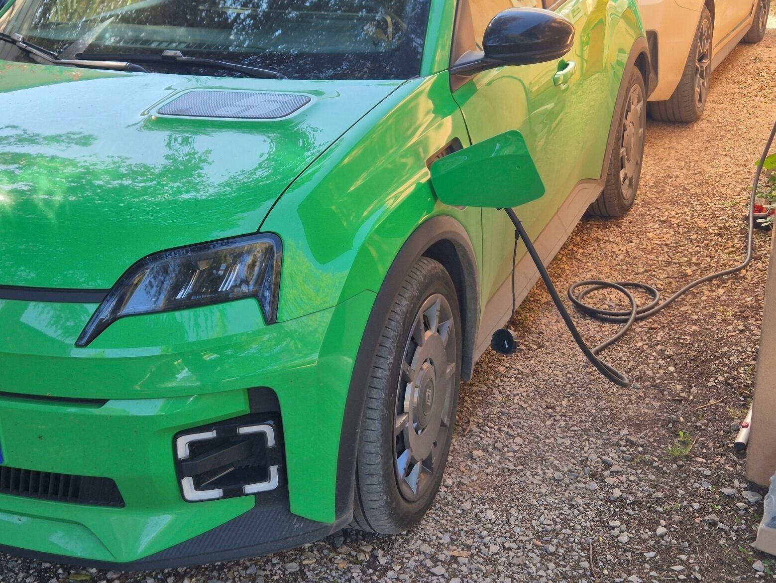 Un coche verde estacionado sobre grava con un cable de carga conectado.