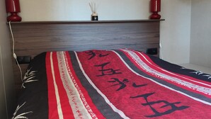 Una cama con una colcha de cuadros rojo y negro, un cabecero de madera y dos lámparas de noche rojas.