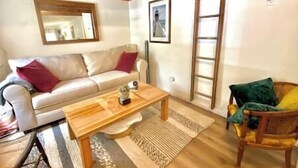 A living room with a sofa, a wooden coffee table, a wicker chair, and a ladder against the wall. - Aloft in Acadia National Park (Mount Desert)