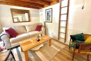 A living room with a sofa, a wooden coffee table, a wicker chair, and a ladder against the wall. - Aloft in Acadia National Park (Mount Desert)