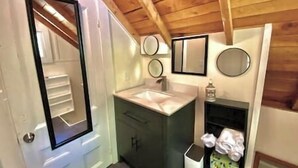 A bathroom with a wooden ceiling, a white door, a sink, and a mirror. - Aloft in Acadia National Park (Mount Desert)