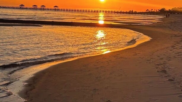 Una playa al atardecer con un muelle de madera que se adentra en el agua.