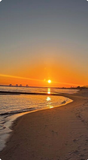 Uma praia ao pôr do sol com um píer de madeira que se estende sobre a água.