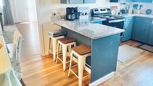 Una cocina con isla central, taburetes de bar y una estación para café.